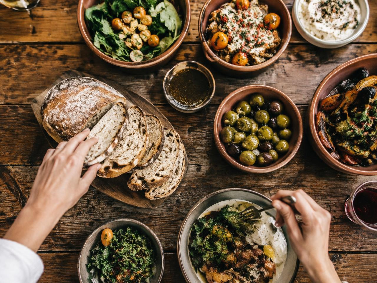 Hands reaching for bread and shared dishes on a wooden table
